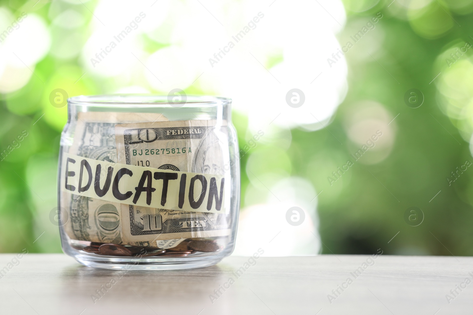 Photo of Glass jar with money and label EDUCATION on table against blurred background. Space for text