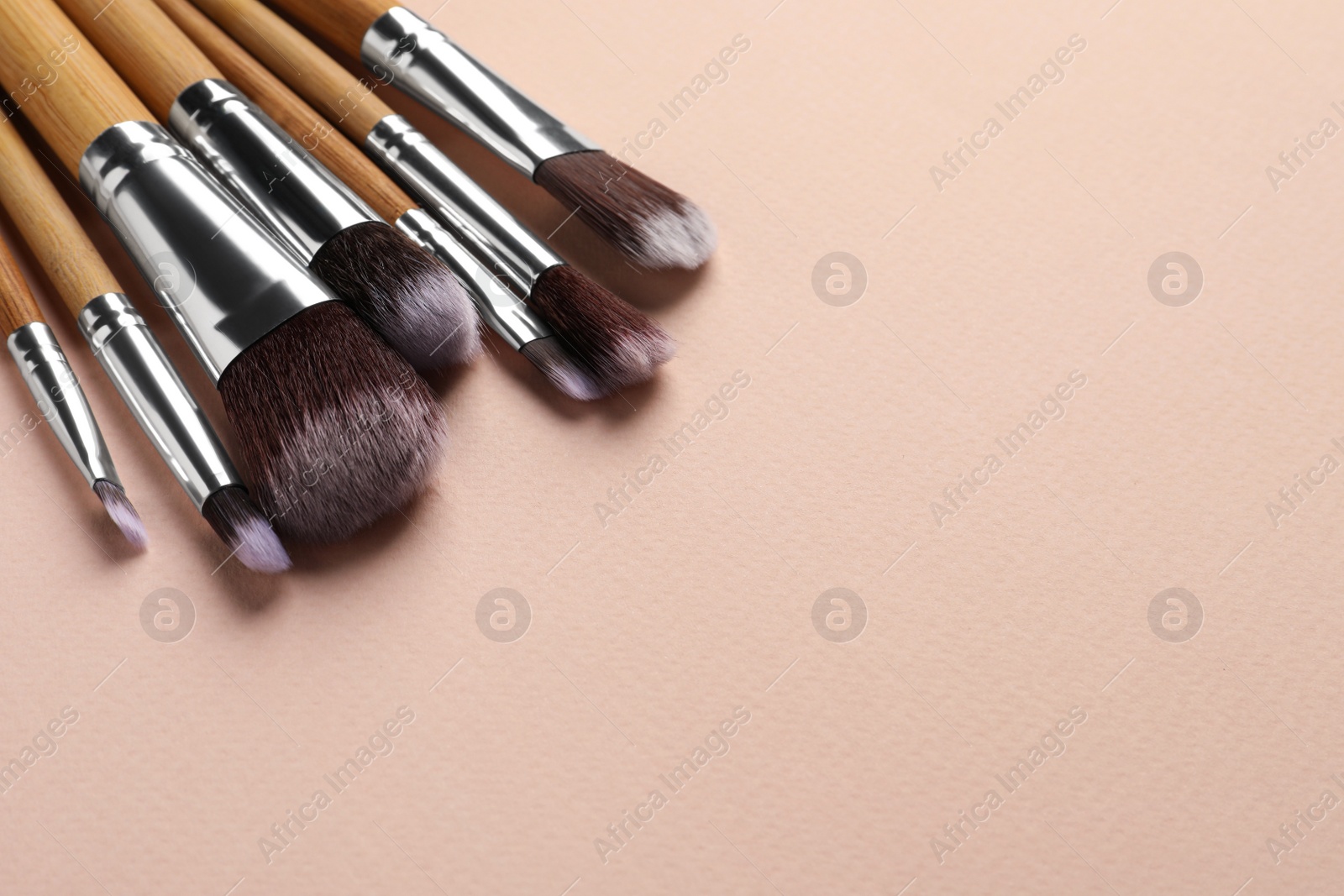 Photo of Set of makeup brushes on beige background, space for text