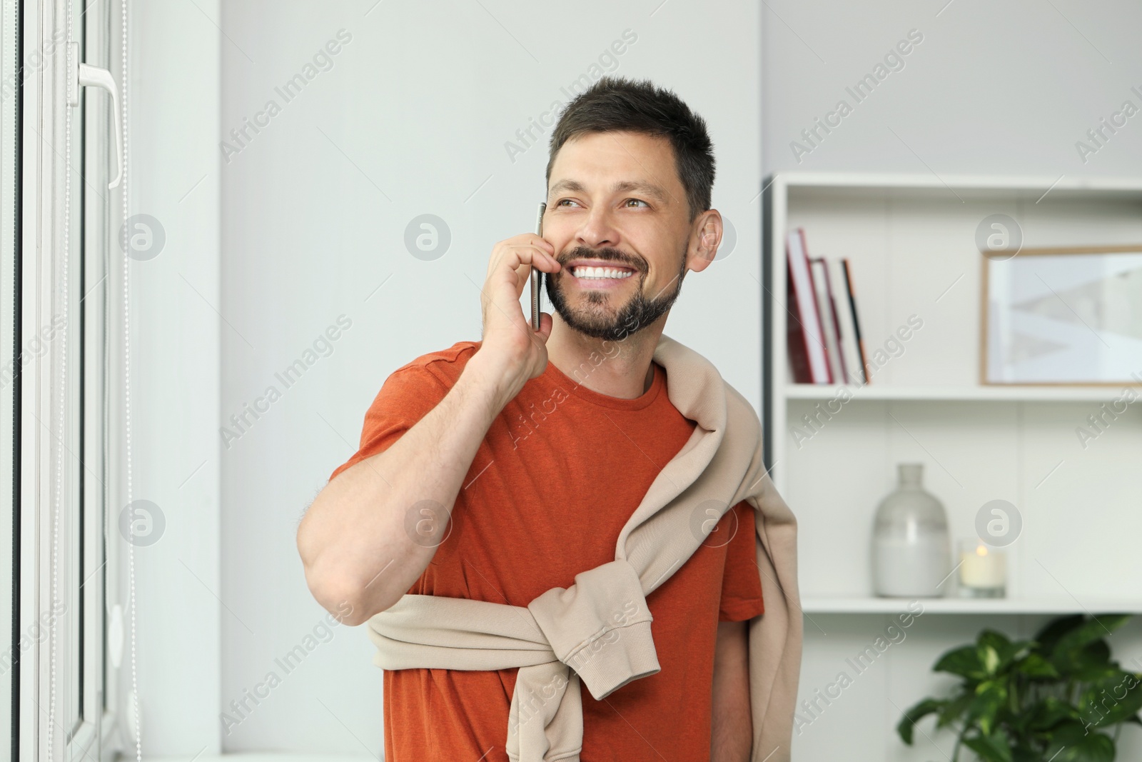 Photo of Happy man talking on smartphone at home