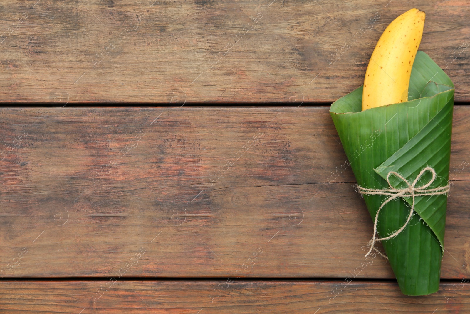 Photo of Delicious ripe banana wrapped in fresh leaf on wooden table, top view. Space for text