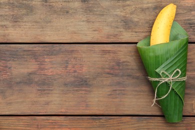 Photo of Delicious ripe banana wrapped in fresh leaf on wooden table, top view. Space for text