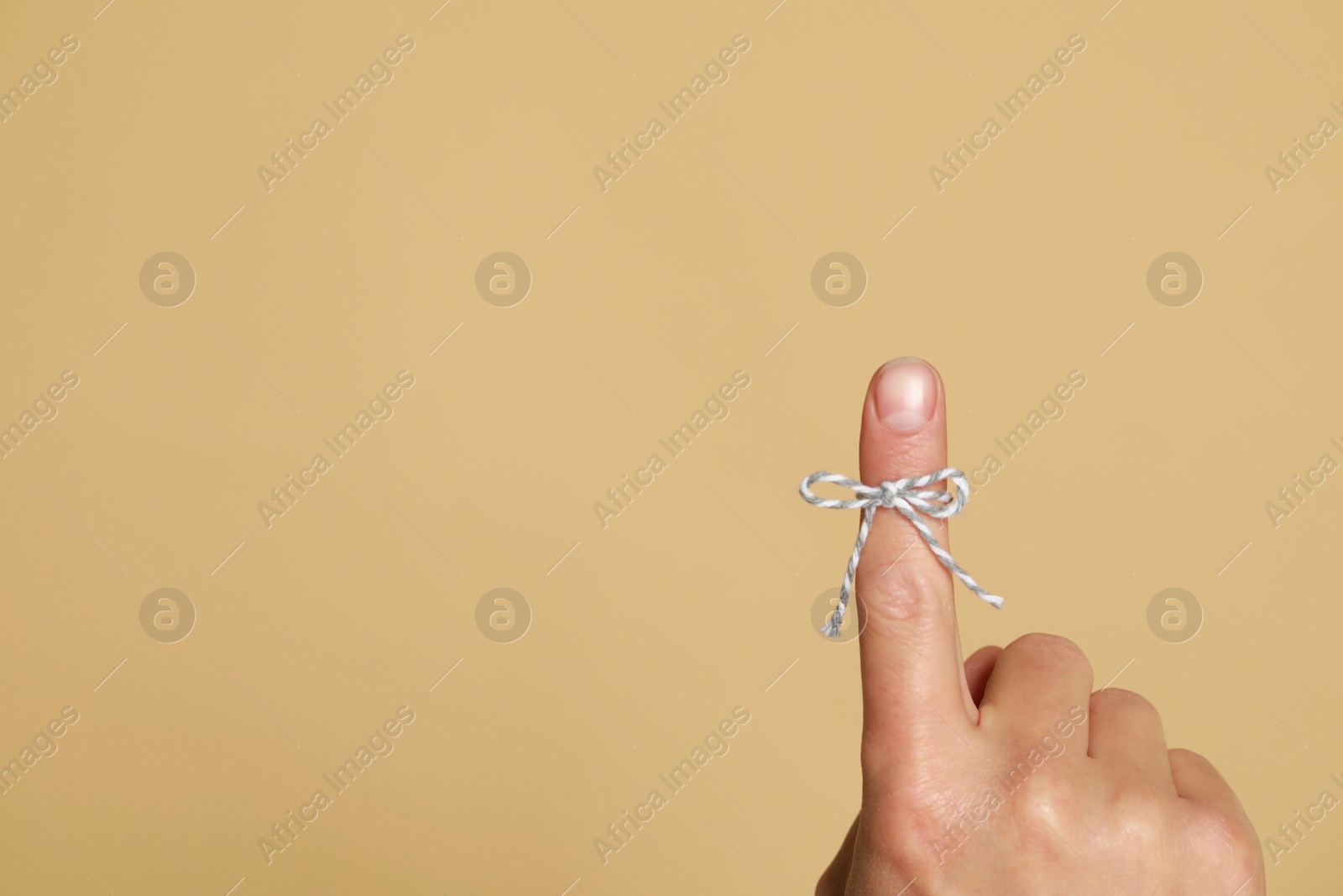 Photo of Man showing index finger with tied bow as reminder on beige background, closeup. Space for text