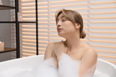 Beautiful woman taking bath with foam in tub indoors