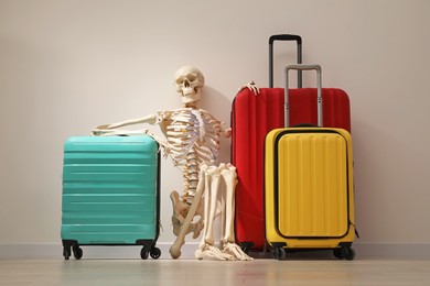 Waiting concept. Human skeleton with suitcases near light grey wall