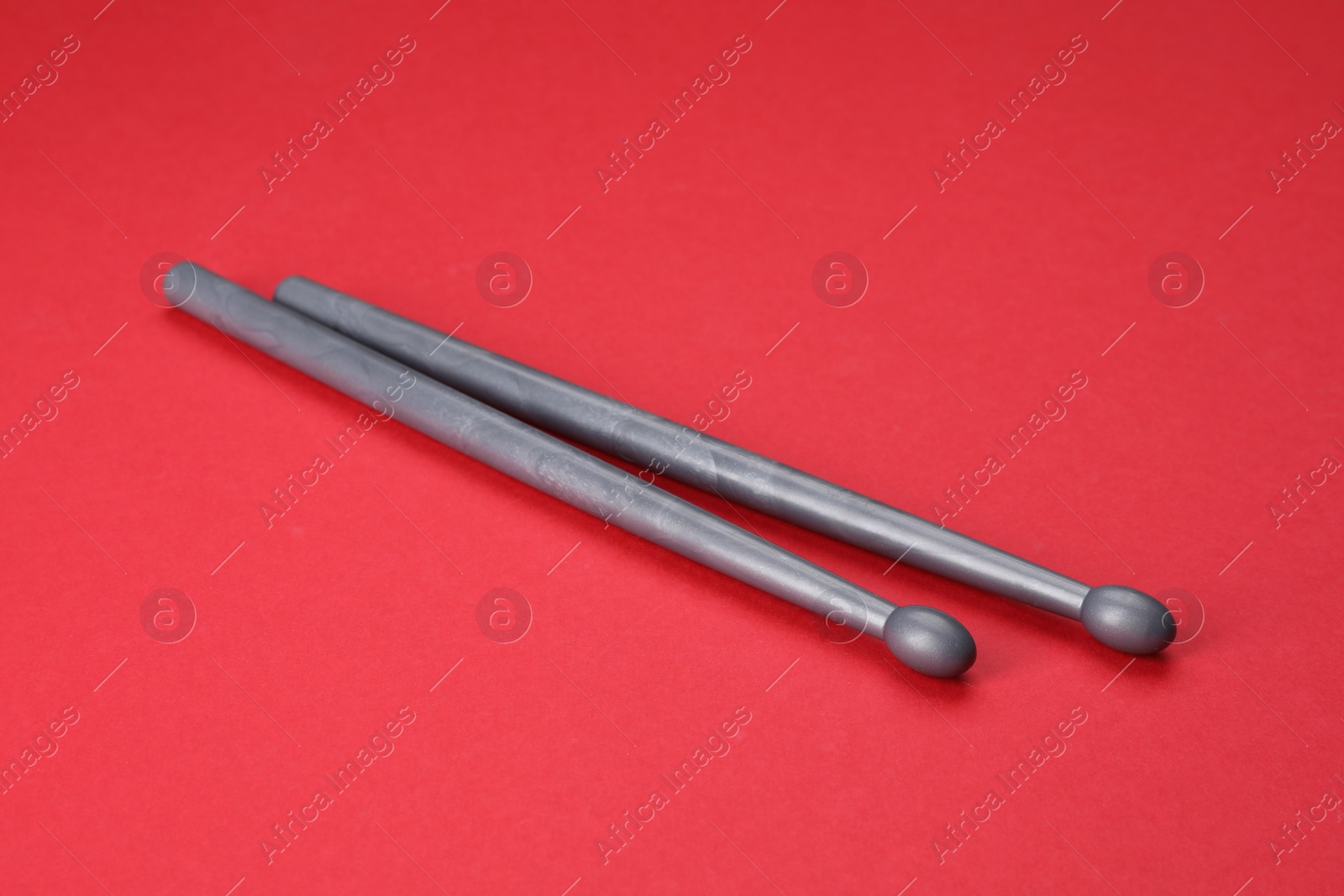 Photo of Two gray drum sticks on red background