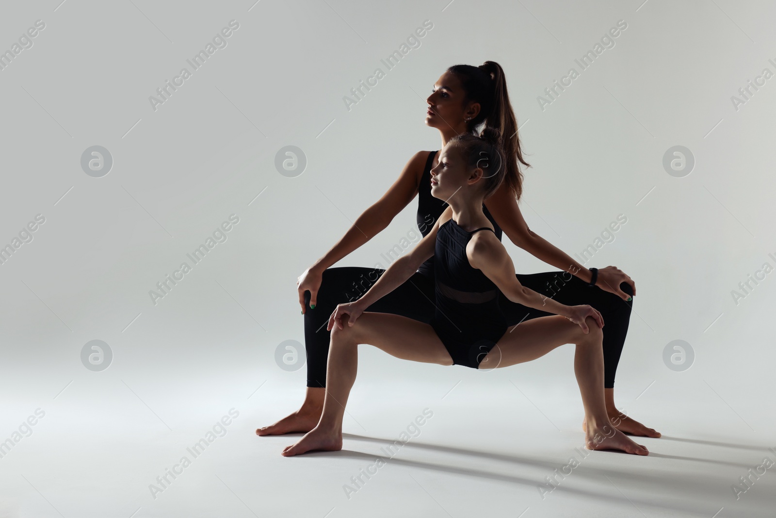 Photo of Little girl and her coach doing gymnastic exercise on white background