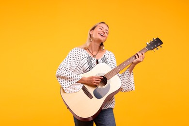 Photo of Happy hippie woman playing guitar on yellow background