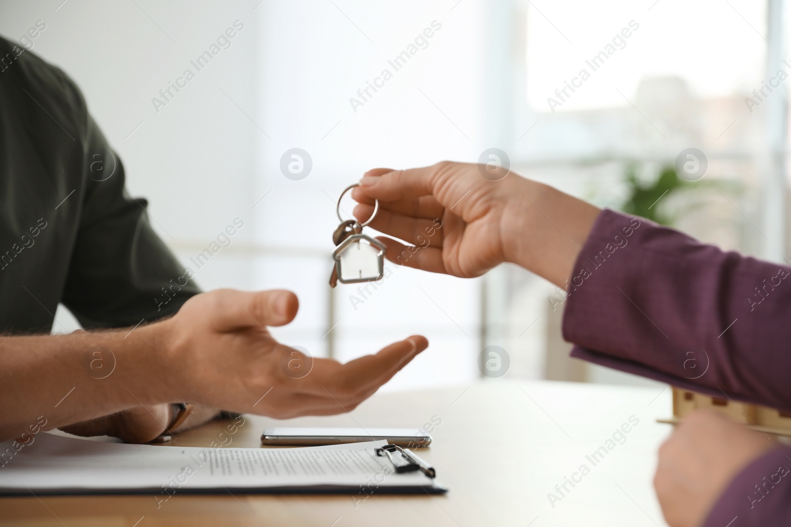 Photo of Real estate agent giving key with trinket to client in office, closeup