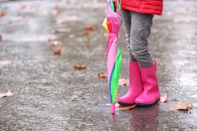 Photo of Little girl with rubber boots and umbrella after rain, focus of legs. Autumn walk