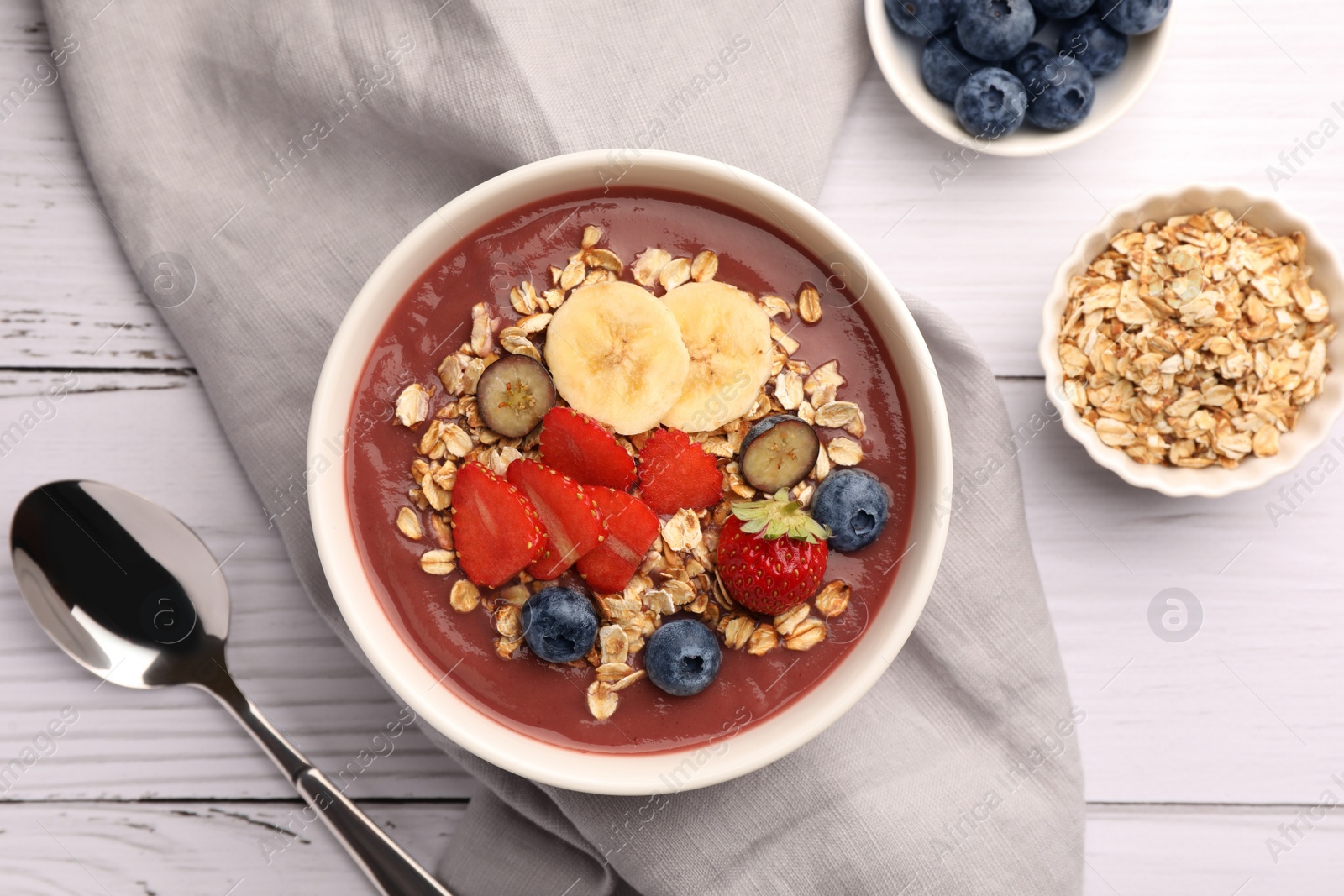 Photo of Delicious smoothie bowl with fresh berries, banana and granola on white wooden table, flat lay
