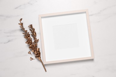 Empty photo frame and golden dried flowers on white marble background, flat lay. Space for design