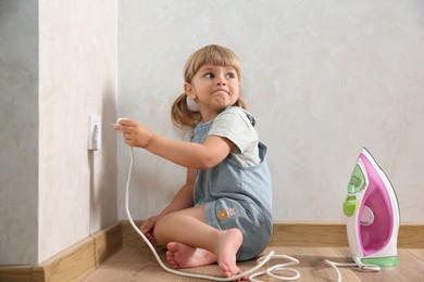 Little child playing with electrical socket and iron plug at home. Dangerous situation