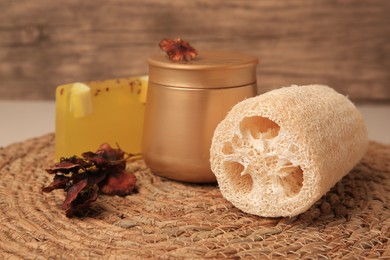 Photo of Natural loofah sponge and cosmetic products on wicker mat, closeup