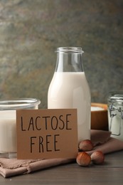Photo of Milk in glassware, card with phrase Lactose free and hazelnuts on wooden table