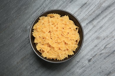 Photo of Raw farfalle pasta in bowl on grey table, top view