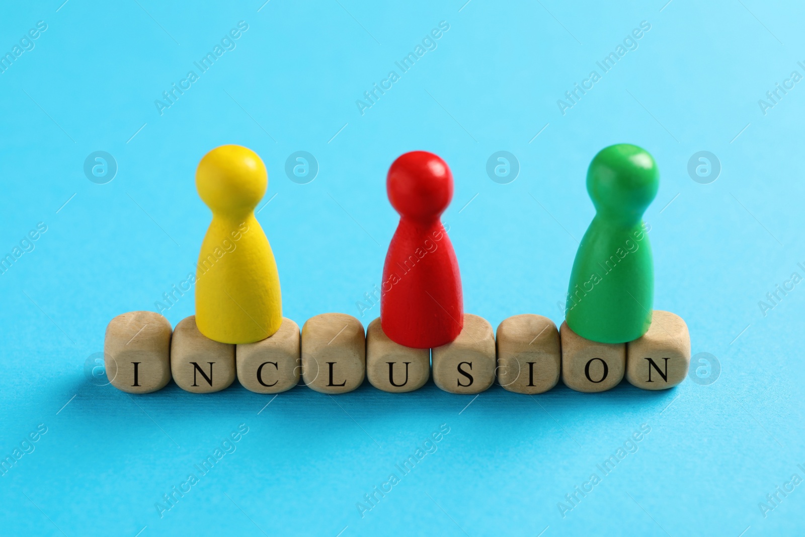 Photo of Colorful pawns and wooden cubes with word Inclusion on light blue background, closeup