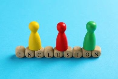 Photo of Colorful pawns and wooden cubes with word Inclusion on light blue background, closeup