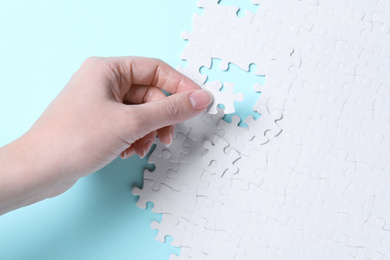 Photo of Woman putting together white puzzle on light blue background, closeup