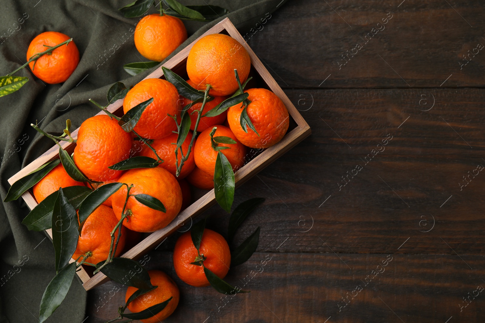 Photo of Fresh ripe tangerines with green leaves in crate on wooden table, top view. Space for text