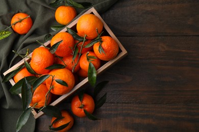 Photo of Fresh ripe tangerines with green leaves in crate on wooden table, top view. Space for text