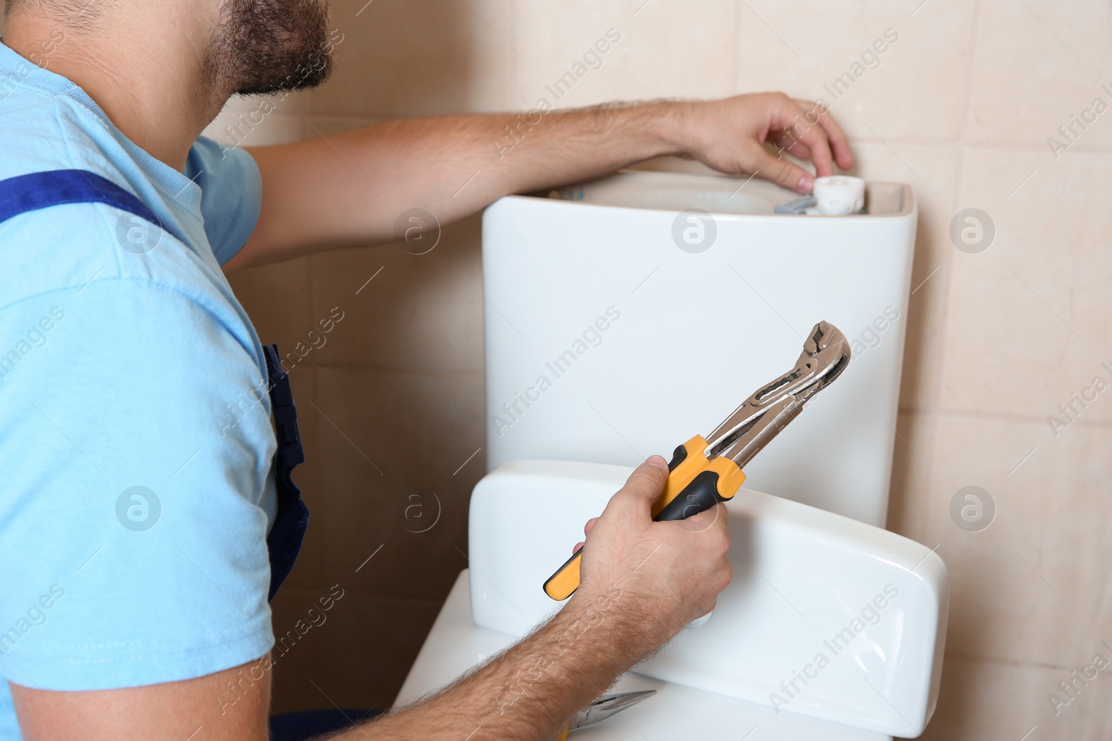 Photo of Professional plumber repairing toilet tank indoors, closeup