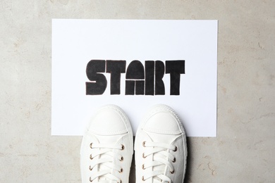 Photo of Sheet of paper with word Start and stylish sneakers on grey table, flat lay