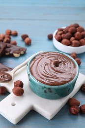 Photo of Bowl with tasty paste, chocolate pieces and nuts on light blue wooden table