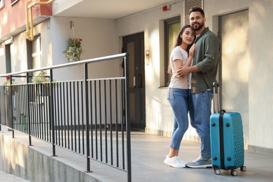 Photo of Long-distance relationship. Beautiful young couple and suitcase near house entrance outdoors