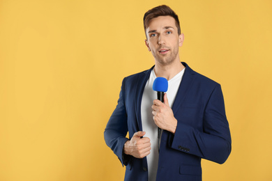 Photo of Young male journalist with microphone on yellow background. Space for text