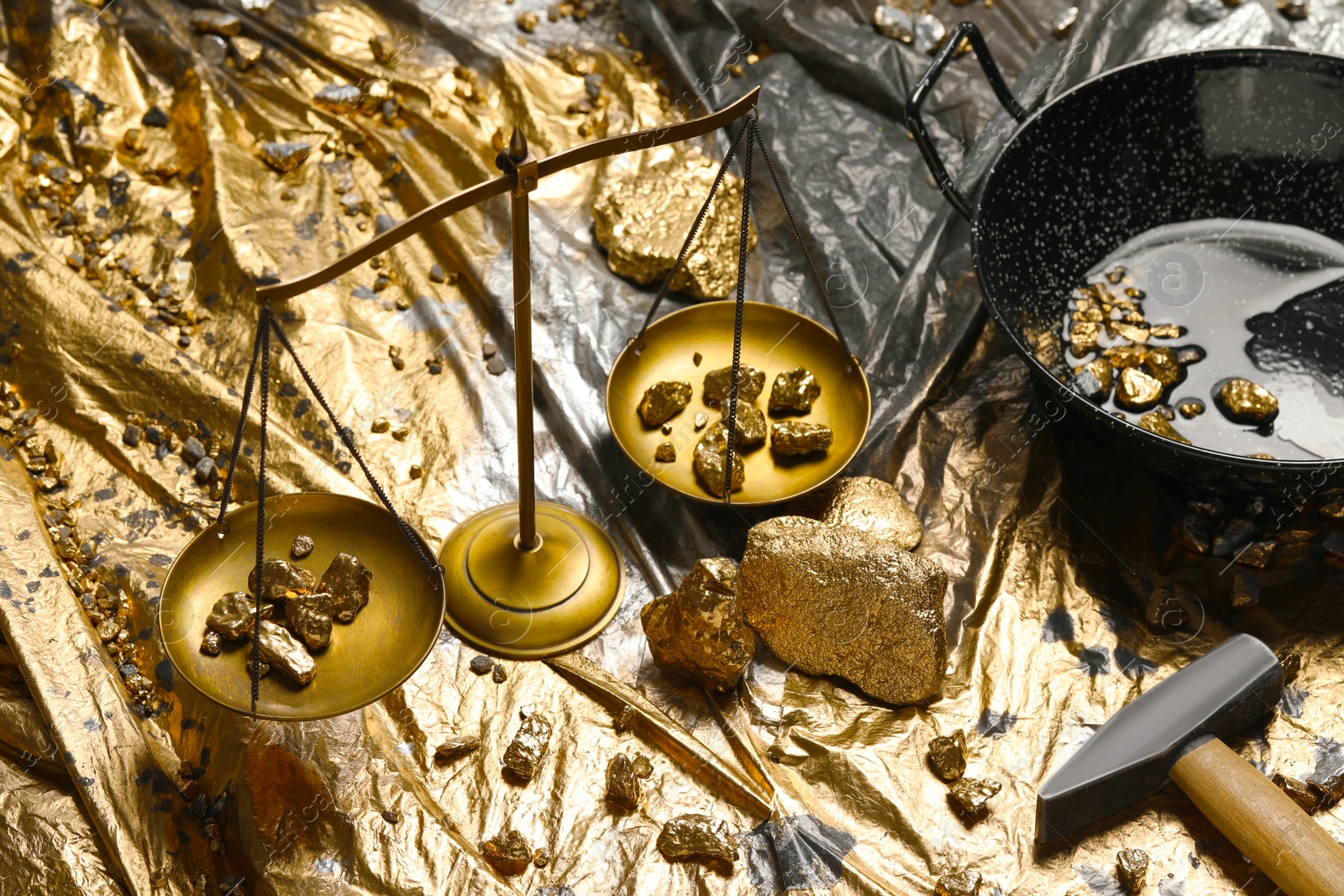 Photo of Gold nuggets, vintage scales, hammer and wok on plastic stretch wrap