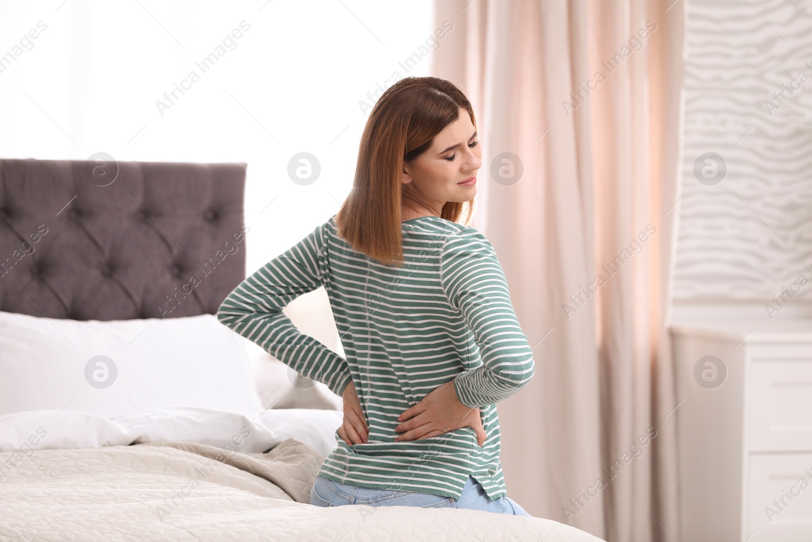 Photo of Young woman suffering from back pain at home