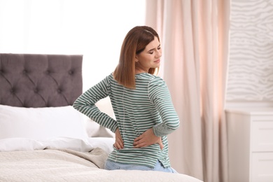 Photo of Young woman suffering from back pain at home