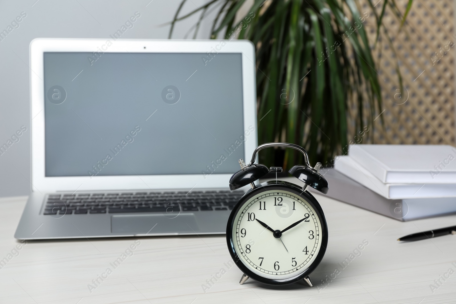 Photo of Laptop, notebooks, pen and alarm clock on white wooden table indoors