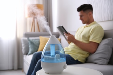 Photo of Modern air humidifier and blurred man on background