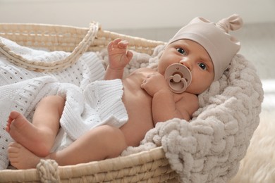 Adorable newborn baby with pacifier in wicker basket indoors