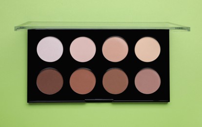 Photo of Colorful contouring palette on light green background, top view. Professional cosmetic product