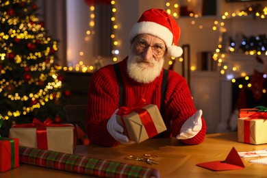 Santa Claus holding gift box at his workplace in room decorated for Christmas