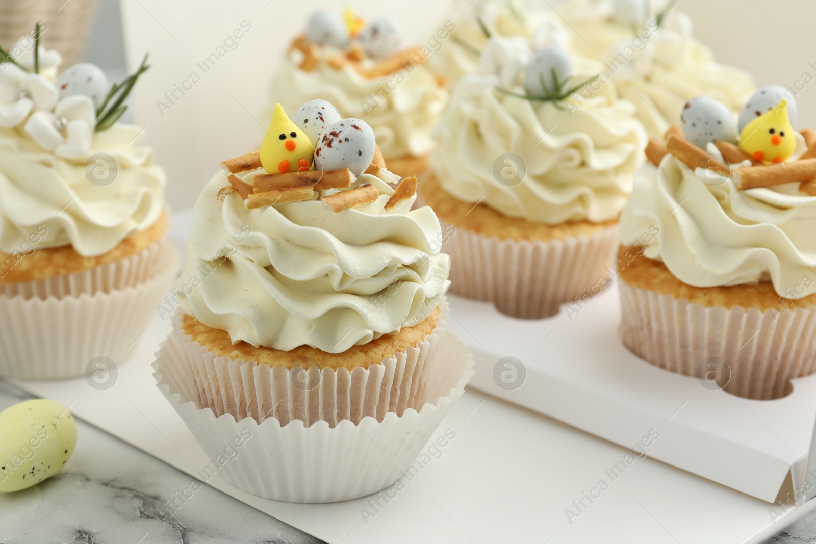 Photo of Tasty Easter cupcakes with vanilla cream on white marble table