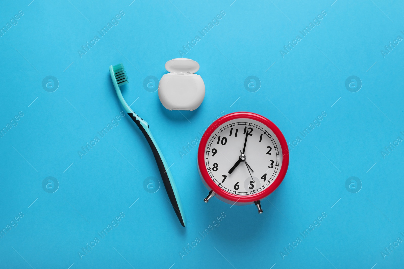 Photo of Container with dental floss, toothbrush and alarm clock on light blue background, flat lay