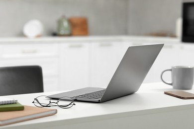 Photo of Home office. Laptop, glasses, smartphone and stationery on white desk in kitchen