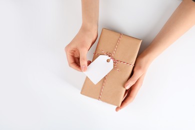 Photo of Woman holding parcel wrapped in kraft paper with tag on white background, top view