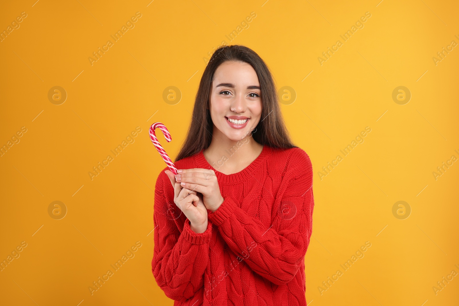 Photo of Young woman in red sweater holding candy cane on yellow background. Celebrating Christmas