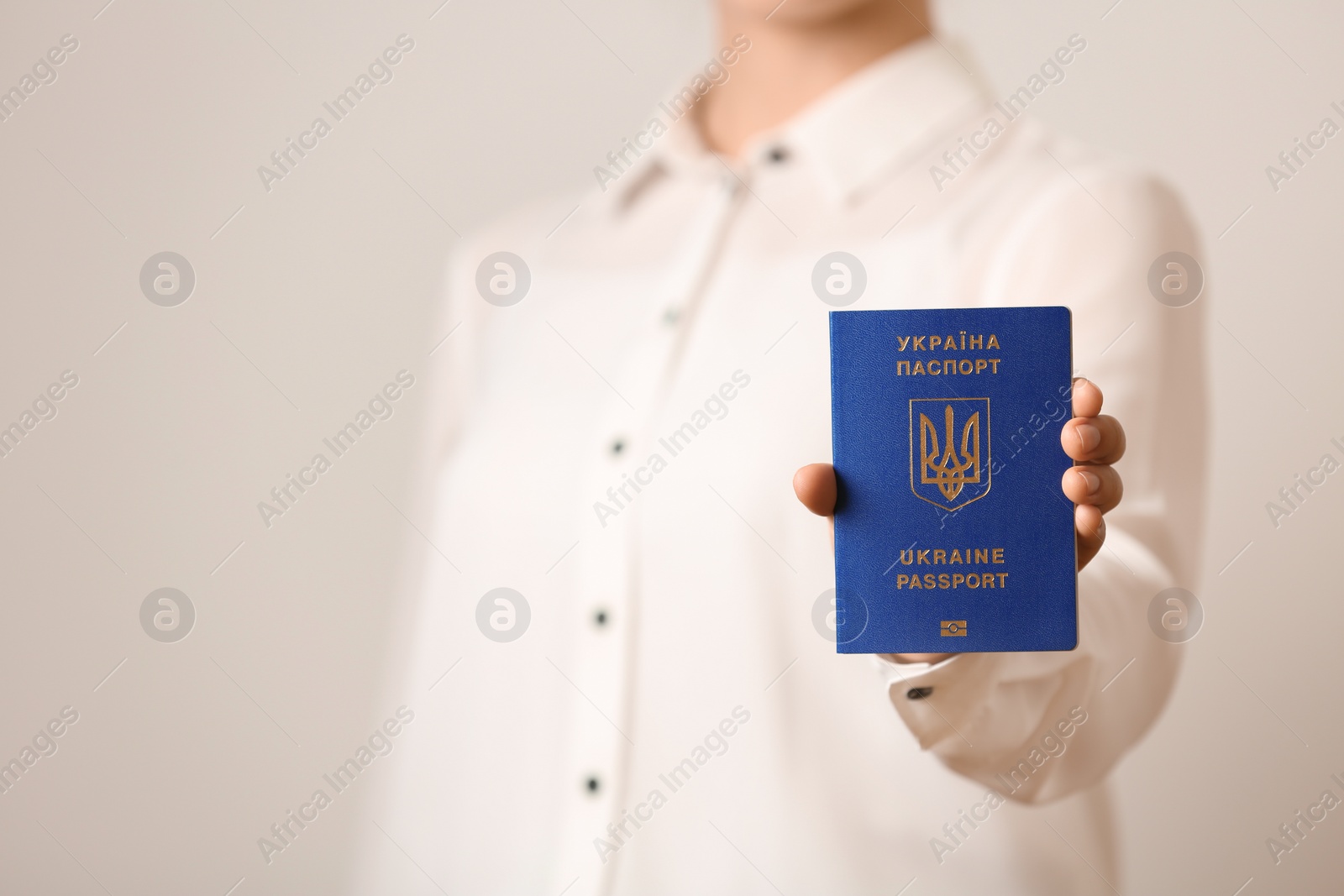 Photo of Woman holding Ukrainian travel passport on light background, closeup with space for text. International relationships