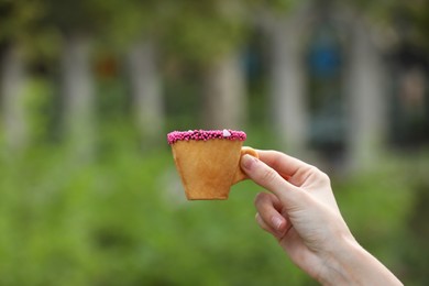Photo of Woman holding delicious edible biscuit cup of coffee decorated with sprinkles outdoors, closeup