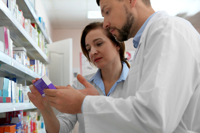 Professional pharmacists near shelves in modern drugstore