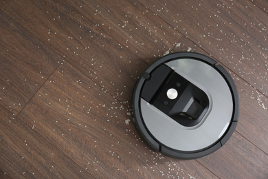 Modern robotic vacuum cleaner removing scattered rice from wooden floor, top view. Space for text