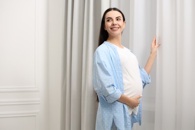 Happy pregnant woman near window indoors, space for text