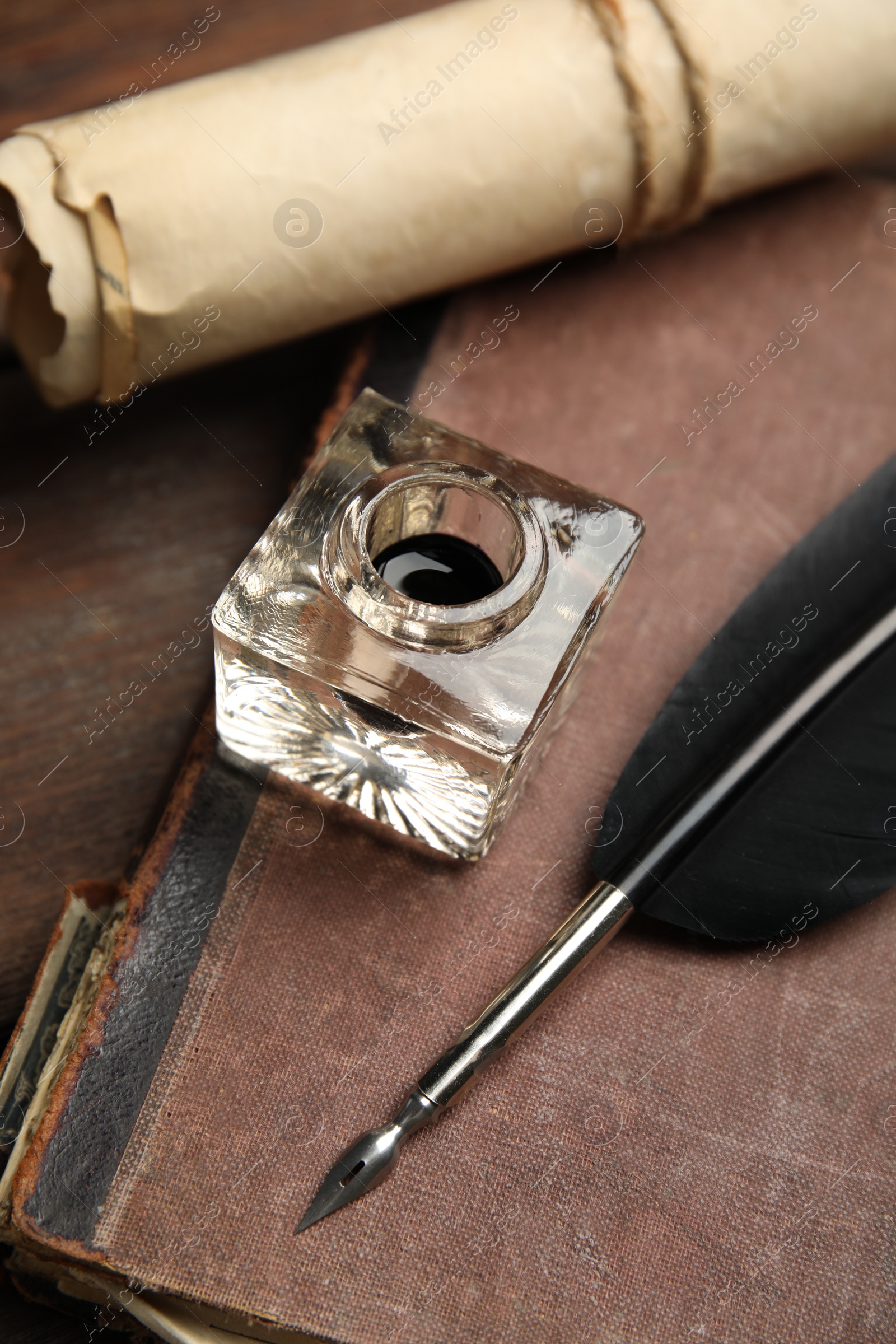 Photo of Feather pen, inkwell, old book and parchment scroll on wooden table, closeup