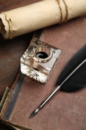 Feather pen, inkwell, old book and parchment scroll on wooden table, closeup