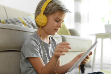 Photo of Cute little boy with headphones and tablet listening to audiobook at home